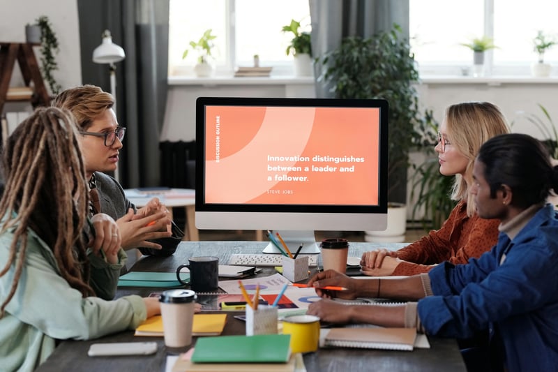 Four teachers are sitting around a conference table facing a big computer screen which shows a presentation slide.