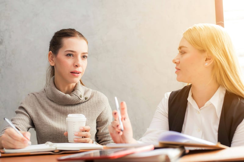 Two teachers are sitting side by side in a meeting with one teacher explaining a concept to the other in what seems to be a follow up or mentorship meeting.