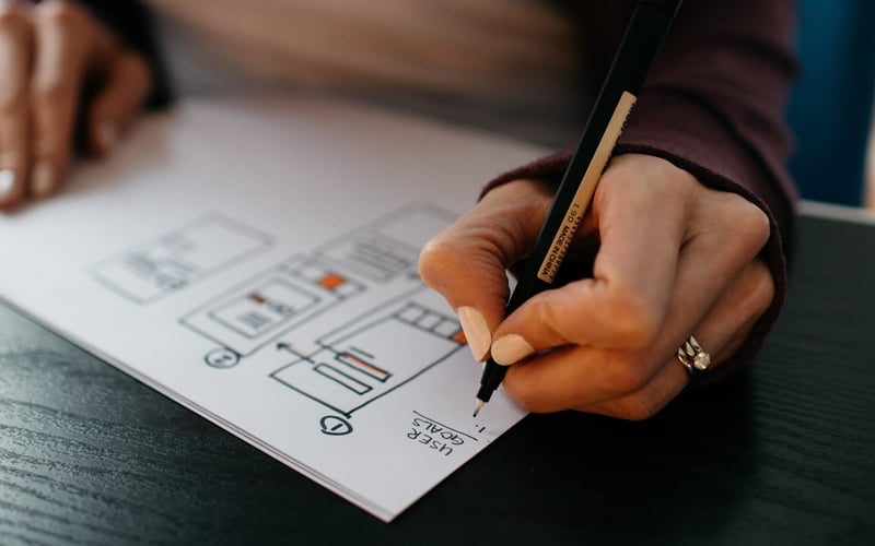 Close-up of a teacher’s hand writing goals and tracking job applications to stay organized during the job search.