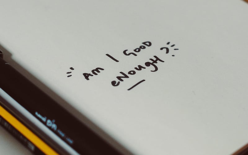 Handwritten question "Am I good enough?" on a notebook, symbolizing self-doubt during the teacher job search process.