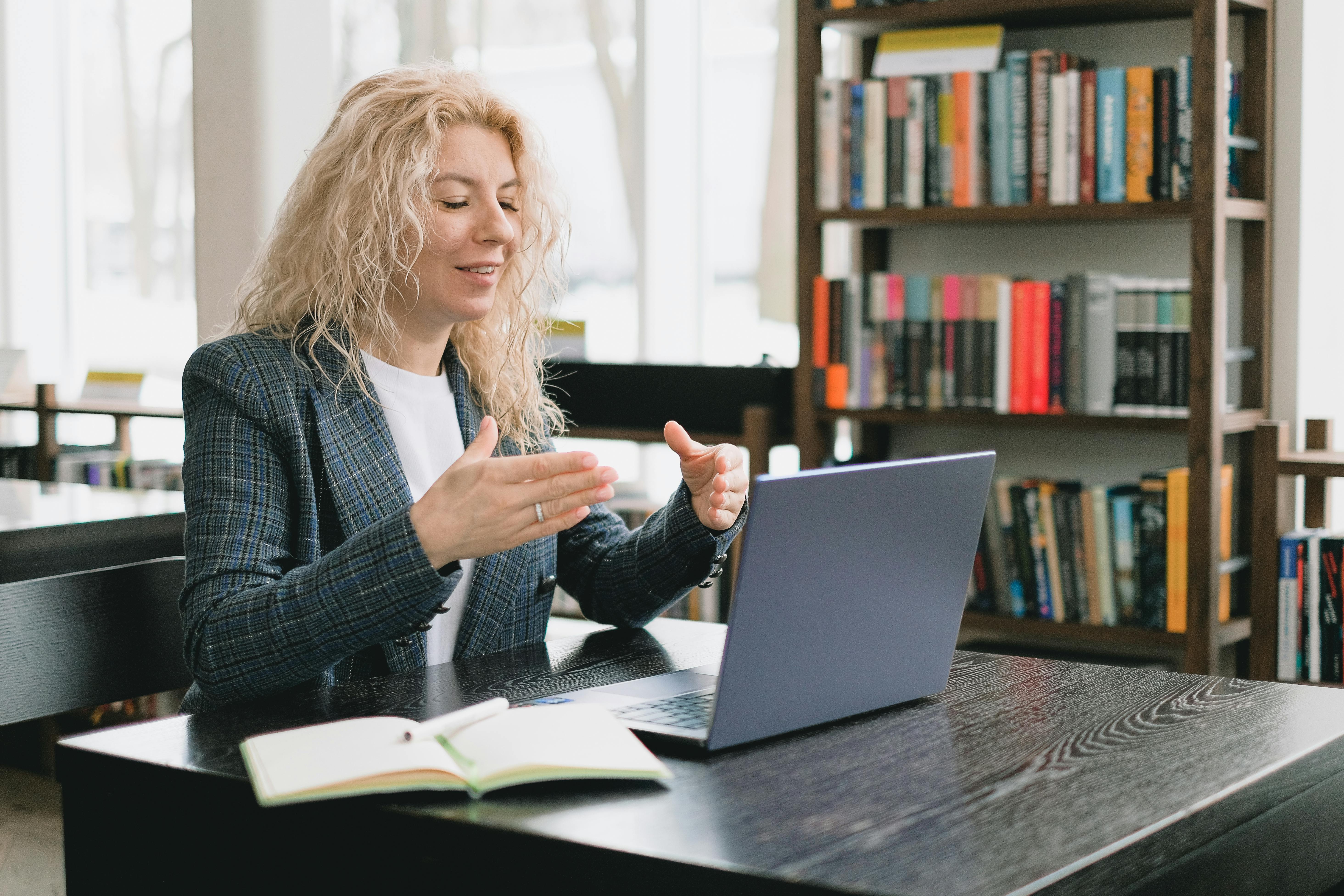 Teacher sitting on a desk with an open laptop, giving an online class