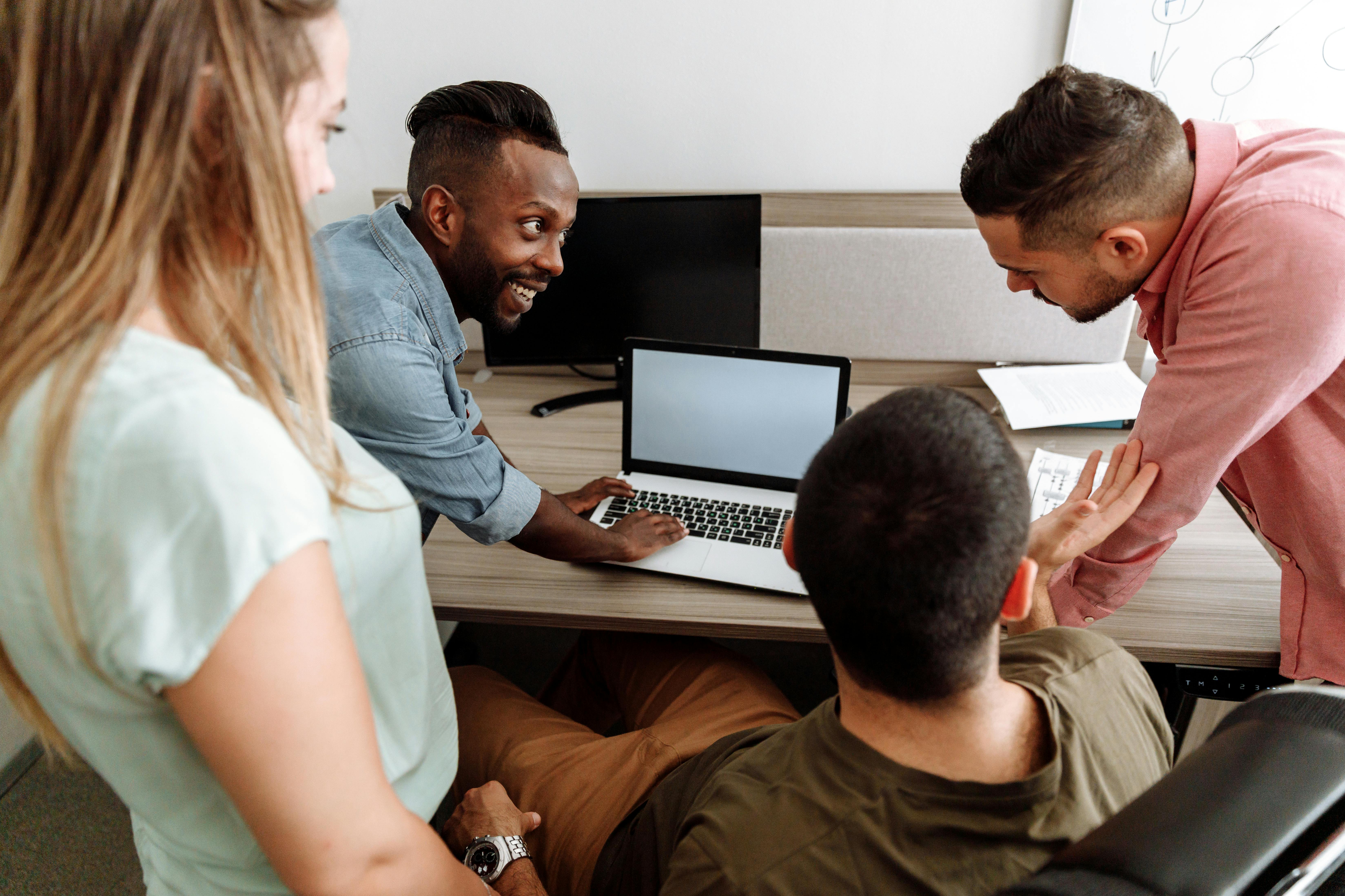 A group of four adults gathered around a laptop