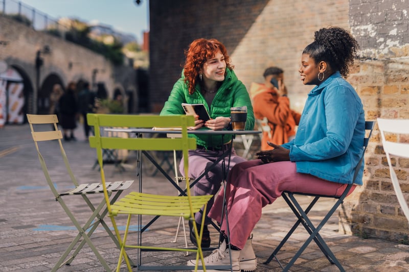 Two educators having a supportive conversation at a cafe, emphasizing the importance of connection during job hunting.